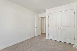 Unfurnished bedroom featuring light carpet and a closet