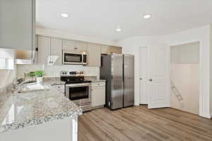 Kitchen featuring light stone counters, stainless steel appliances, sink, and light hardwood / wood-style flooring