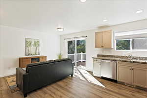 Kitchen with light stone counters, sink, light hardwood / wood-style floors, and dishwasher