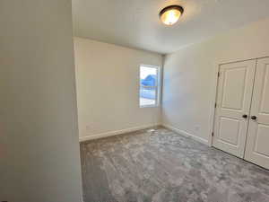 Unfurnished bedroom with carpet, a closet, a textured ceiling, and baseboards