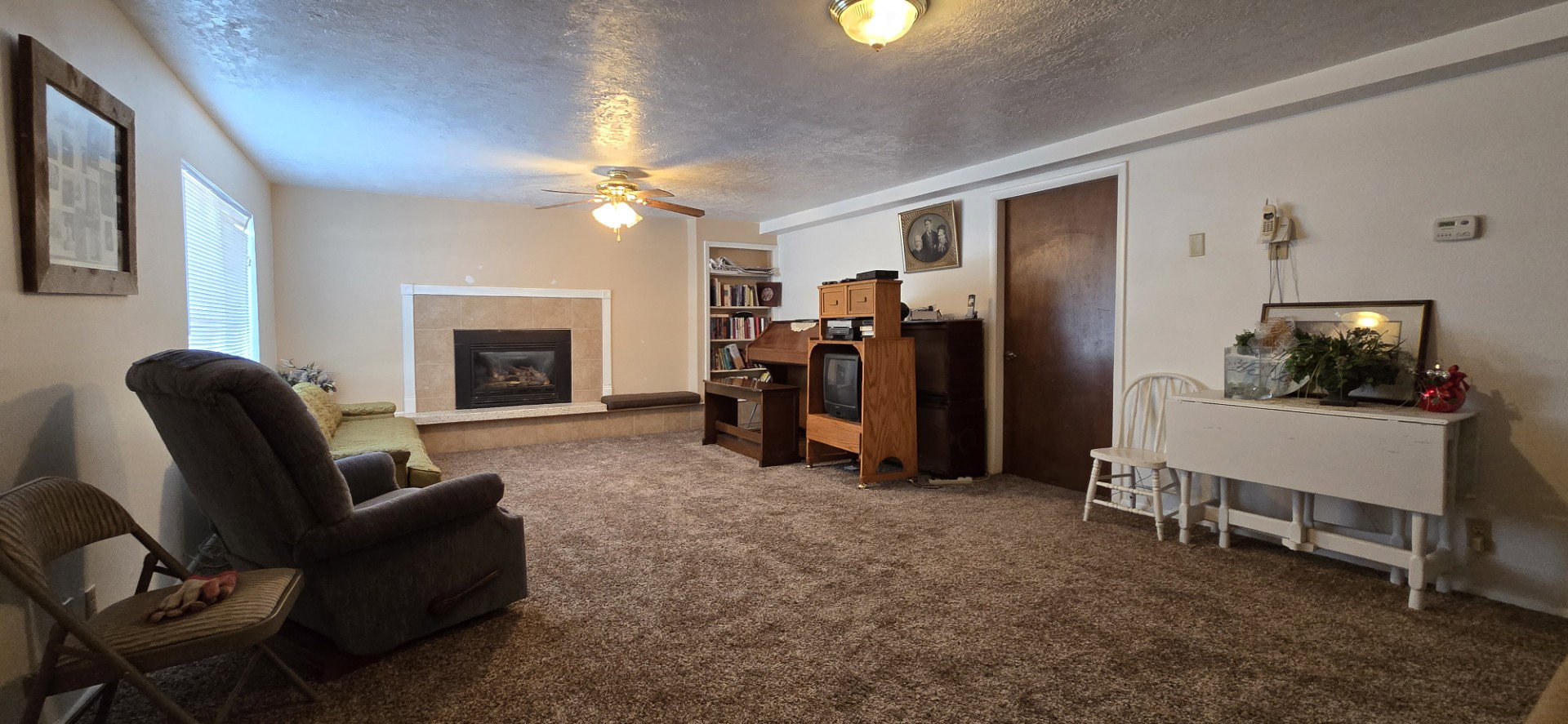 Carpeted living room with ceiling fan, a tiled fireplace, and a textured ceiling