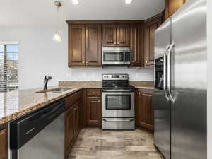 Kitchen with sink, hanging light fixtures, stainless steel appliances, light stone countertops, and kitchen peninsula