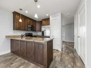 Kitchen with hanging light fixtures, light stone countertops, appliances with stainless steel finishes, and kitchen peninsula