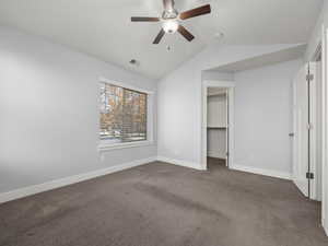 Unfurnished bedroom featuring lofted ceiling, a spacious closet, dark carpet, a closet, and ceiling fan