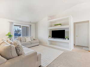 Living room with vaulted ceiling, light colored carpet, and built in features