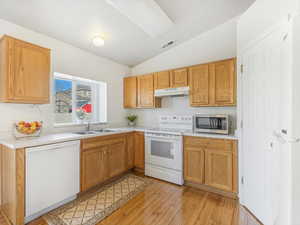 Kitchen with sink, white appliances, vaulted ceiling, and light wood-type flooring