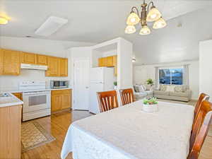 Dining area featuring an inviting chandelier, vaulted ceiling, and light wood-type flooring