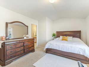 Carpeted bedroom featuring lofted ceiling and ensuite bathroom