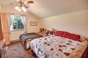 Bedroom featuring vaulted ceiling, a textured ceiling, baseboard heating, carpet floors, and ceiling fan