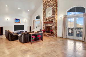 Great room featuring a stone fireplace, high vaulted ceiling, and french doors to covered deck.