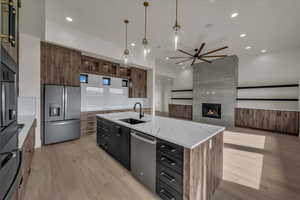 Kitchen featuring appliances with stainless steel finishes, an island with sink, sink, light hardwood / wood-style floors, and light stone countertops