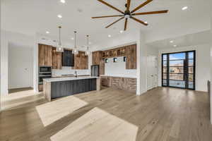 Kitchen featuring light hardwood / wood-style flooring, an island with sink, pendant lighting, ceiling fan, and stainless steel appliances