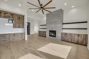 Unfurnished living room with ceiling fan, a fireplace, and light hardwood / wood-style flooring