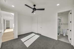 Unfurnished bedroom with dark colored carpet, connected bathroom, and ceiling fan