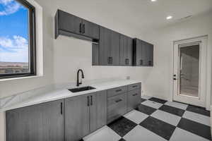 Kitchen with gray cabinetry, sink, and light stone countertops