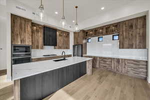 Kitchen with sink, appliances with stainless steel finishes, light stone countertops, light hardwood / wood-style floors, and decorative light fixtures