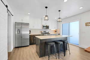 Kitchen with sink, appliances with stainless steel finishes, white cabinets, a center island with sink, and a barn door