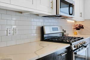 Kitchen with tasteful backsplash, light stone counters, stainless steel appliances, and white cabinets