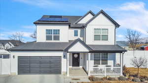 View of front of home with a porch, a garage, and solar panels