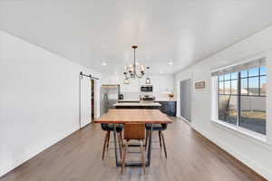 Dining area with a barn door, hardwood / wood-style floors, and a notable chandelier