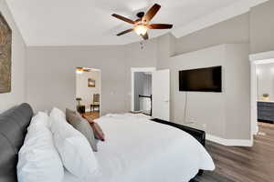 Bedroom with dark wood-type flooring, vaulted ceiling, ensuite bath, and ceiling fan