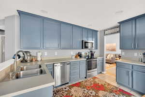 Kitchen with stainless steel appliances, sink, light tile patterned floors, and blue cabinets