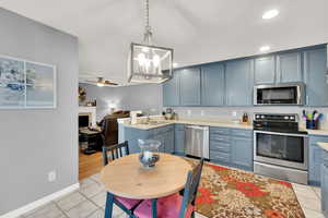 Kitchen featuring blue cabinets, sink, hanging light fixtures, light tile patterned floors, and stainless steel appliances