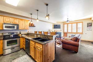 Kitchen with pendant lighting, sink, dark stone countertops, kitchen peninsula, and stainless steel appliances