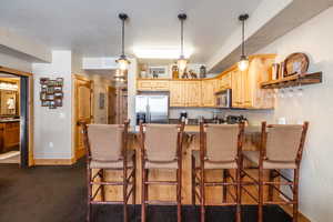 Kitchen with a breakfast bar, dark colored carpet, light brown cabinets, kitchen peninsula, and stainless steel appliances