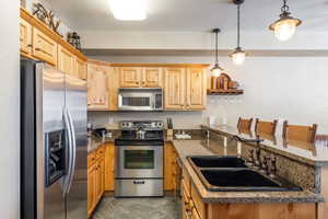 Kitchen with sink, dark stone counters, a kitchen breakfast bar, pendant lighting, and stainless steel appliances