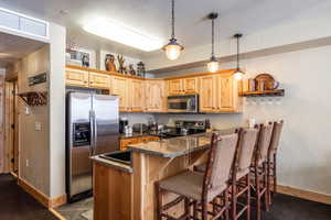 Kitchen with dark tile patterned floors, dark stone countertops, stainless steel appliances, a kitchen bar, and kitchen peninsula