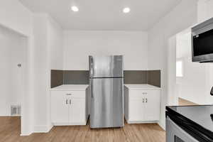 Kitchen with white cabinetry, appliances with stainless steel finishes, and light wood-type flooring