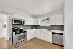 Kitchen with sink, white cabinetry, stainless steel appliances, tasteful backsplash, and light hardwood / wood-style floors