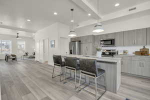 Kitchen with pendant lighting, appliances with stainless steel finishes, an island with sink, a kitchen bar, and light wood-type flooring