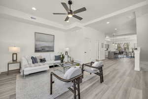 Living room featuring ceiling fan, a tray ceiling, and light hardwood / wood-style flooring