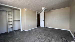 Unfurnished bedroom featuring a textured ceiling, a closet, ceiling fan, and dark colored carpet