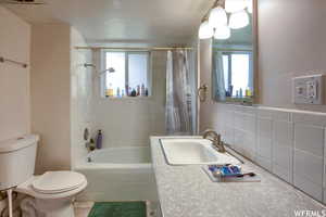 Full bathroom with vanity, tile walls, shower / tub combo, and toilet