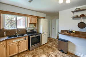 Kitchen featuring stainless steel range with electric stovetop, sink, light brown cabinetry, and white fridge