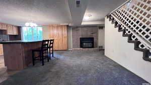 Kitchen featuring hanging light fixtures, a kitchen breakfast bar, dark colored carpet, a fireplace, and light brown cabinets