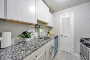 Kitchen with white cabinetry, sink, light tile patterned floors, light stone counters, and stainless steel appliances