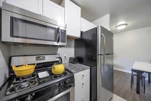 Kitchen featuring white cabinetry, stainless steel appliances, dark hardwood / wood-style flooring, and light stone counters