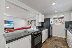 Kitchen with white cabinets, a textured ceiling, and black appliances