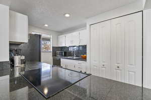 Kitchen with white cabinetry, sink, black dishwasher, and a textured ceiling