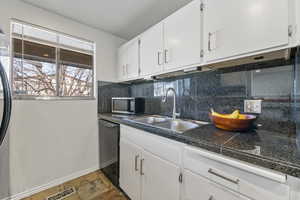 Kitchen with sink, white cabinetry, black dishwasher, tasteful backsplash, and a textured ceiling