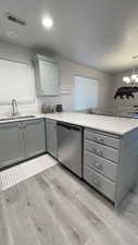 Kitchen featuring sink, light hardwood / wood-style flooring, gray cabinets, dishwasher, and a chandelier