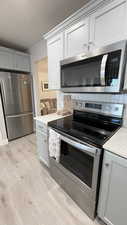 Kitchen with light stone counters, light hardwood / wood-style flooring, and appliances with stainless steel finishes