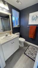 Bathroom featuring wood-type flooring, vanity, an enclosed shower, toilet, and a textured ceiling