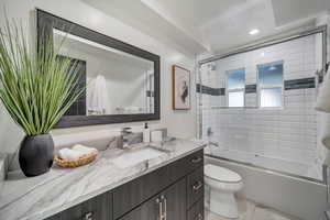 Full bathroom with vanity, toilet, tile patterned floors, and bath / shower combo with glass door