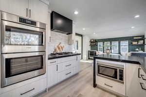 Kitchen featuring wall chimney exhaust hood, tasteful backsplash, light hardwood / wood-style flooring, appliances with stainless steel finishes, and beverage cooler