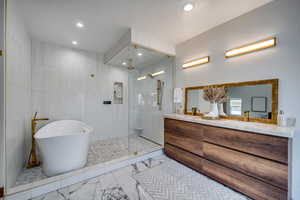 Primary suite bathroom with vanity, separate shower and tub, and tile walls